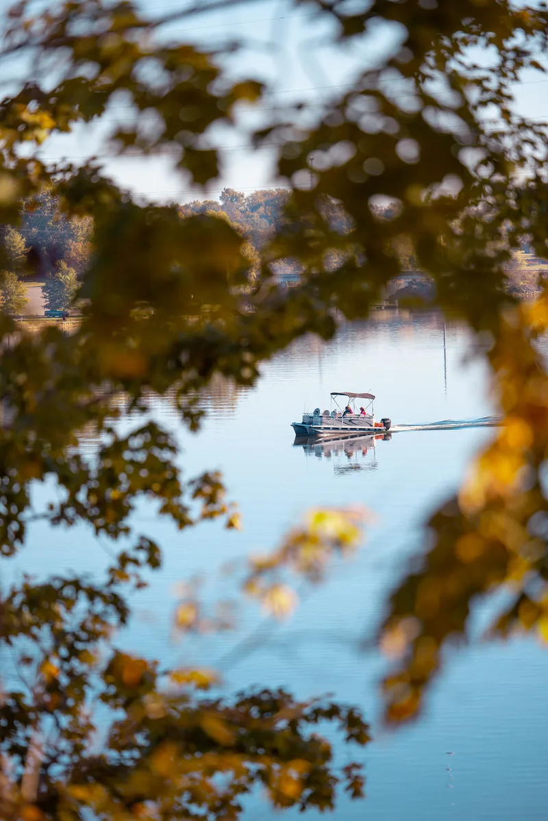 Pontoon boat on calm Tims Ford Lake through autumn leaves